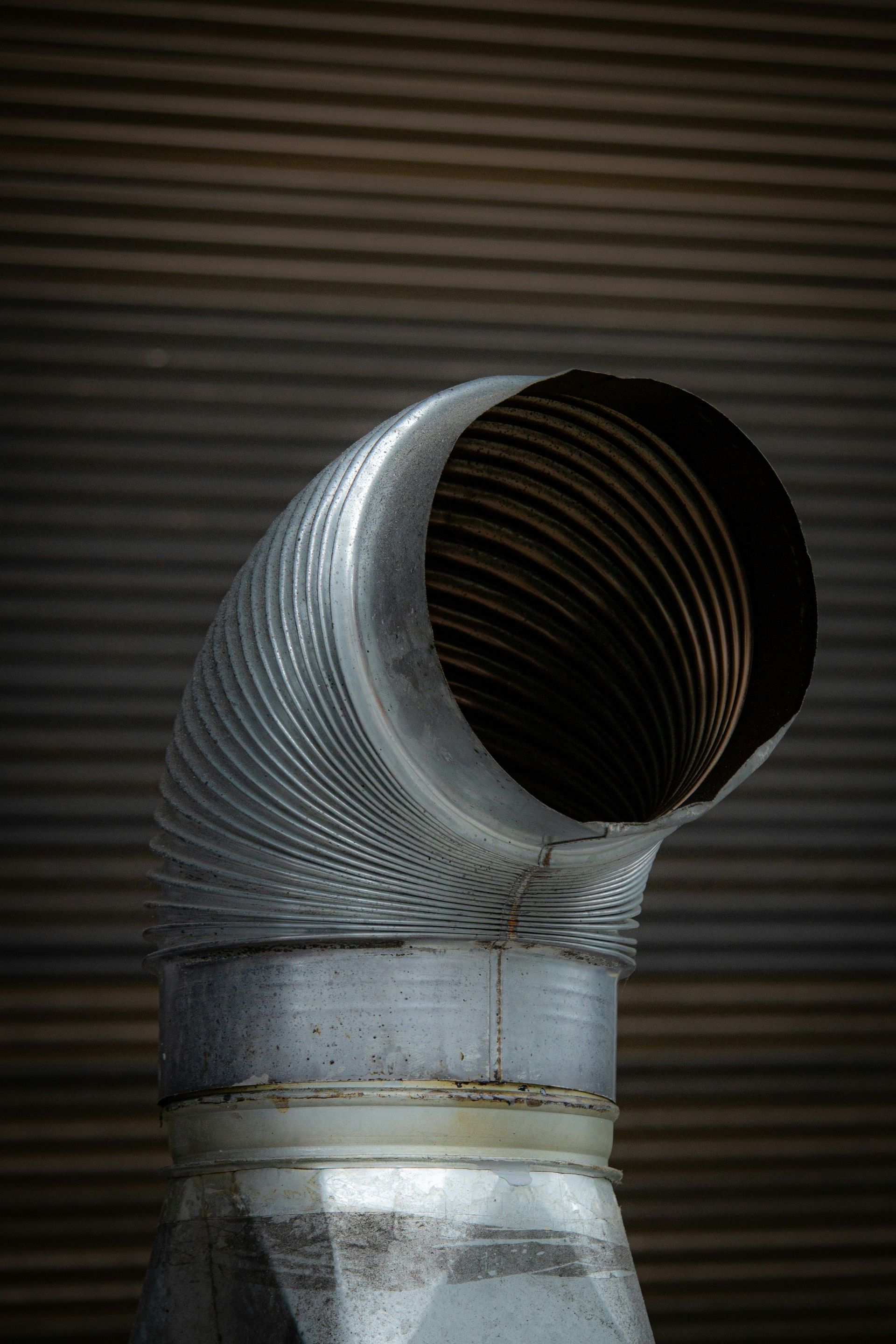 A corrugated metal vent pipe against a textured wall.